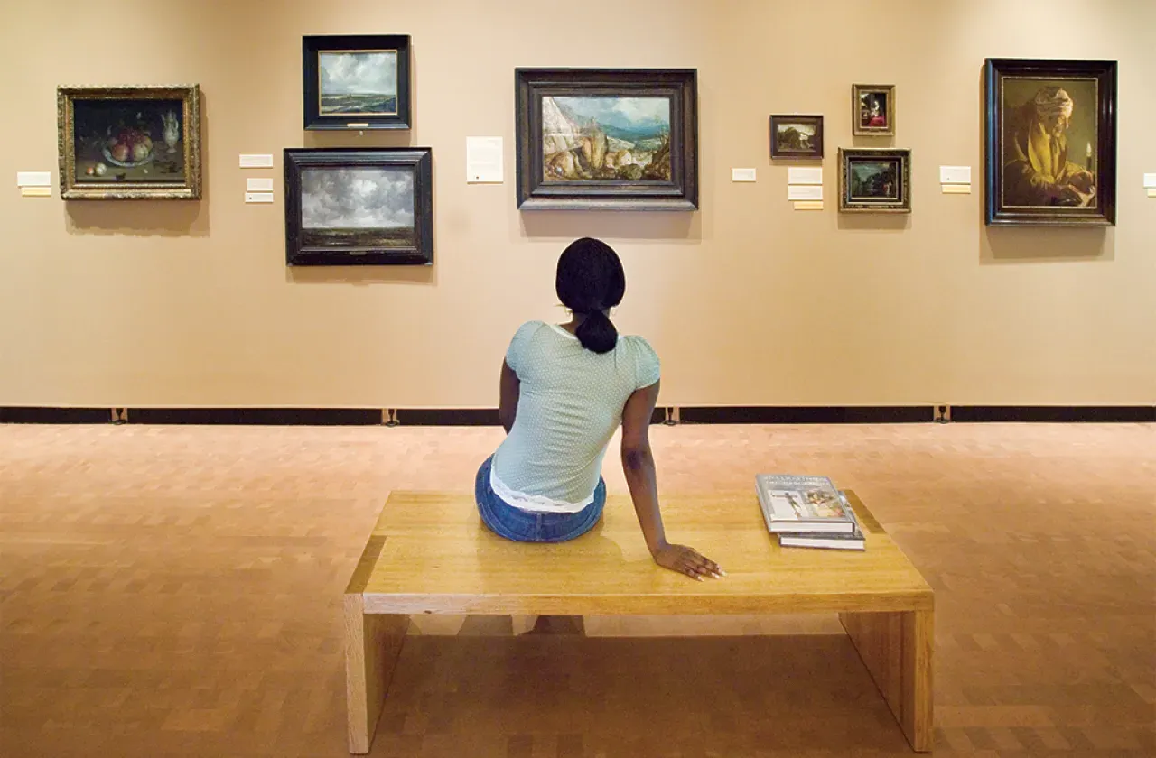 一个学生坐在长凳上看博物馆墙上的画