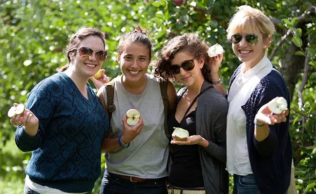 Four students holding half-eaten apples and smiling.