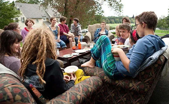 A group of students sitting outside in armchairs, eating breakfast and talking, surrounded by a scenic view.